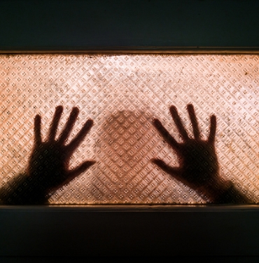 Silhouette Of Domestic Abuse Victim With Hands Pressed Against Glass Window